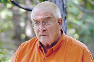 Man wearing glasses and an orange shirt outdoors with blurred greenery
