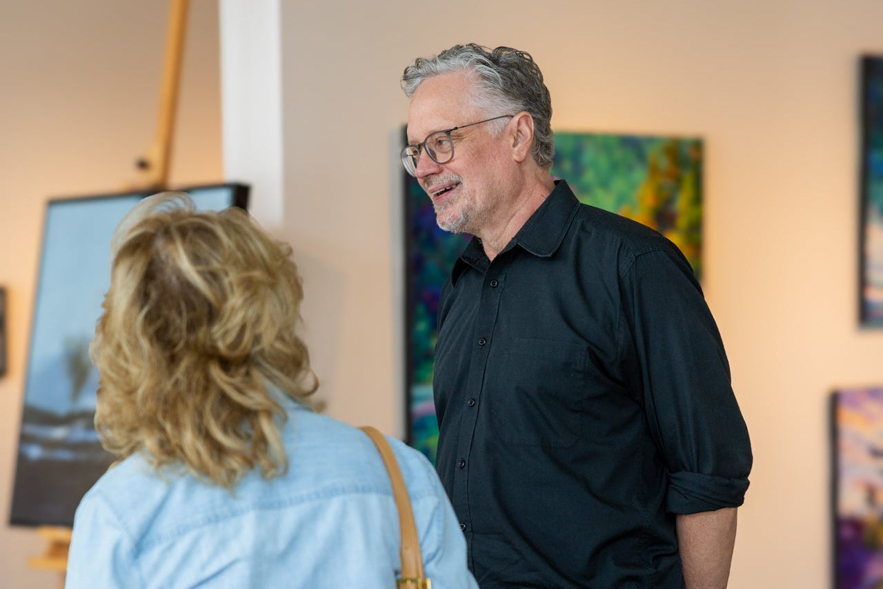 Two people conversing in an art gallery with paintings on the wall.
