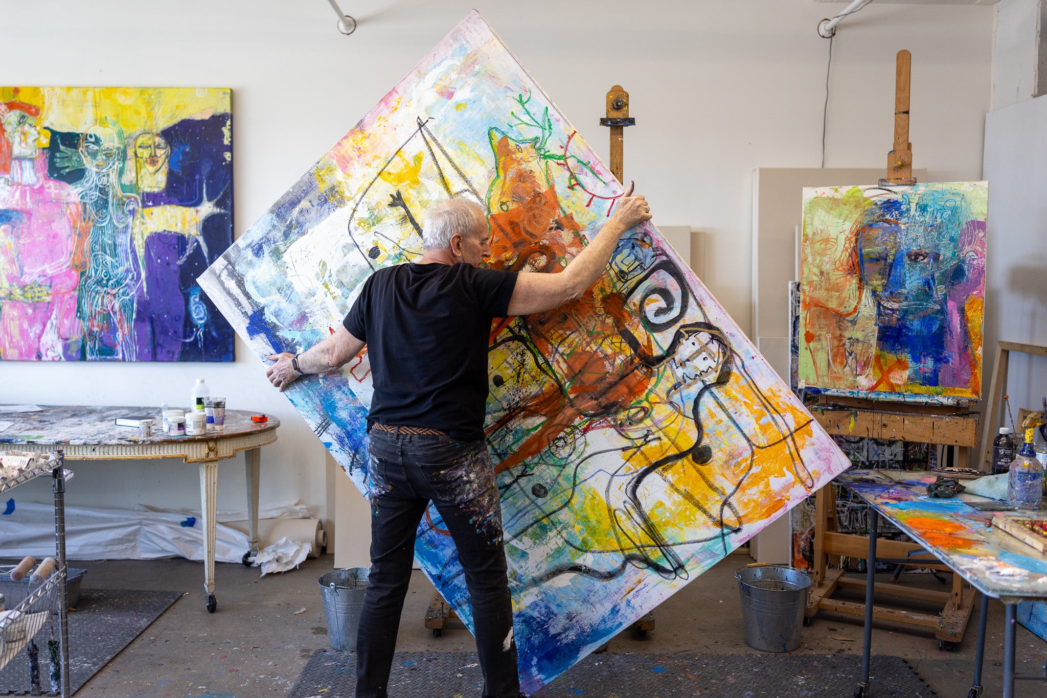 Artist working on a large abstract painting in a studio with other artworks around.