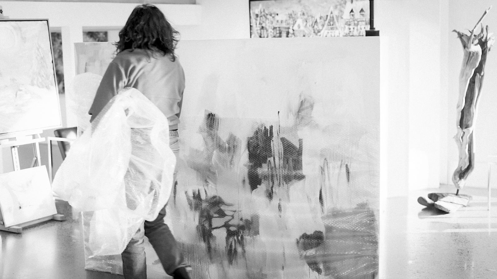 Person standing in front of a large abstract painting with other artworks on the wall.