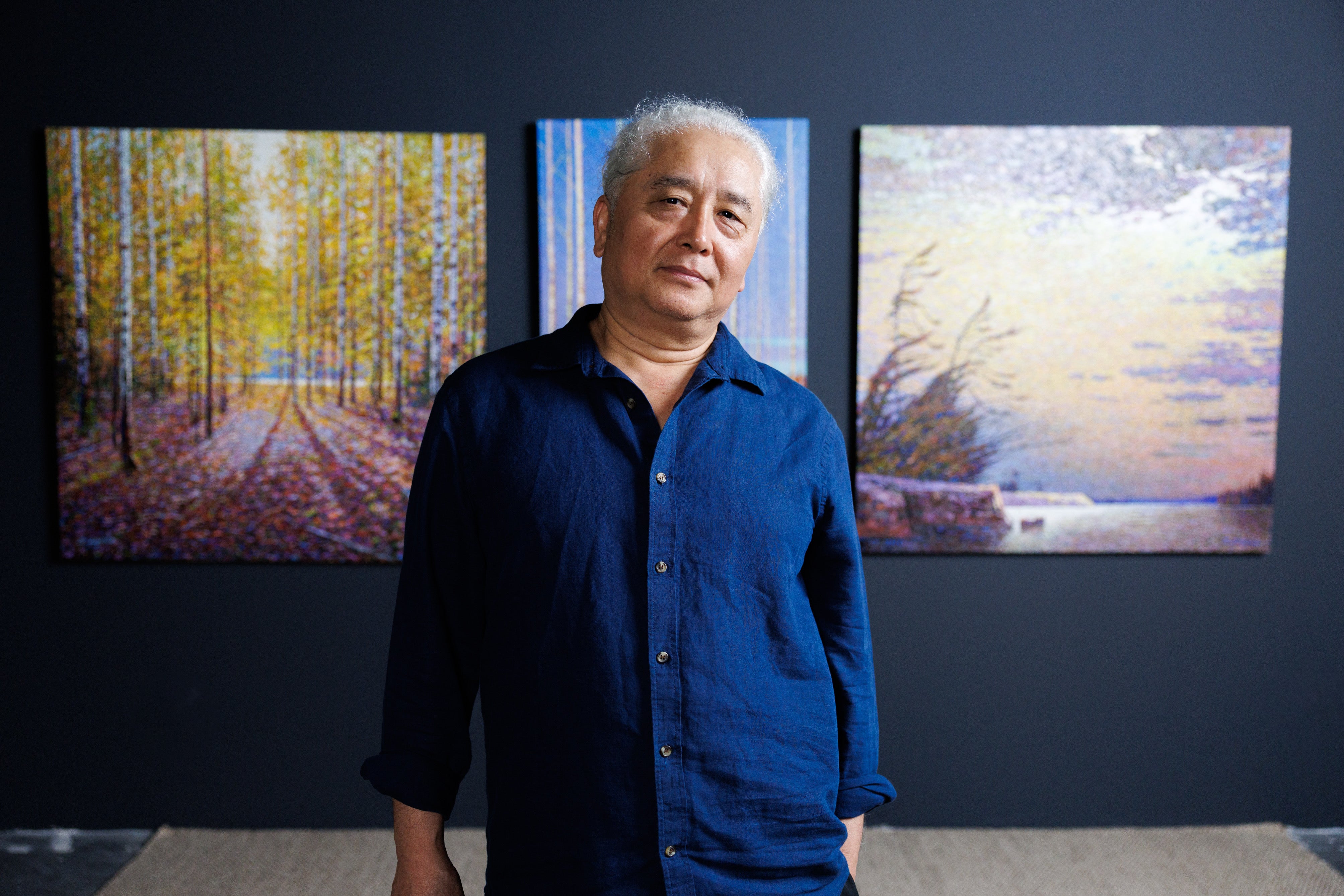 Man standing in front of three colorful abstract paintings on a dark wall.